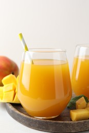 Photo of Tasty mango juice in glasses and fresh fruits on white table, closeup