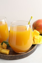 Photo of Tasty mango juice in glasses and fresh fruits on white table, closeup