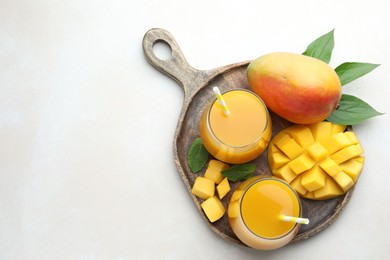 Photo of Tasty mango juice in glasses, fresh fruits, mint and leaves on white table, top view. Space for text