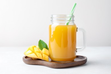 Photo of Tasty mango juice in glass mason jar, fresh fruit and mint on white table