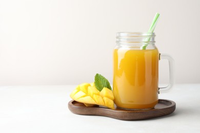Photo of Tasty mango juice in glass mason jar, fresh fruit and mint on white table, space for text