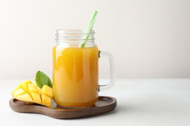 Photo of Tasty mango juice in glass mason jar, fresh fruit and mint on white table, space for text