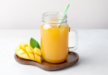 Photo of Tasty mango juice in glass mason jar, fresh fruit and mint on white table