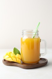 Photo of Tasty mango juice in glass mason jar, fresh fruit and mint on white table