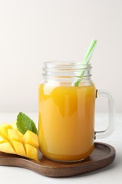 Photo of Tasty mango juice in glass mason jar, fresh fruit and mint on white table, closeup