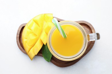 Photo of Tasty mango juice in glass mason jar, fresh fruit and mint on white table, top view
