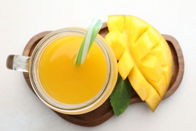 Photo of Tasty mango juice in glass mason jar, fresh fruit and mint on white table, top view