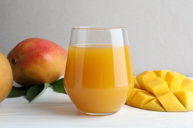 Photo of Tasty mango juice in glass, fresh fruits and green leaves on white wooden table, closeup