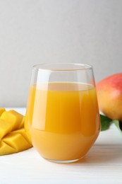 Photo of Tasty mango juice in glass and fresh fruits on white wooden table, closeup
