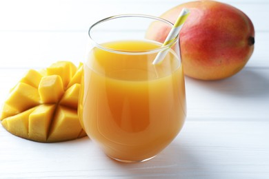 Photo of Tasty mango juice in glass and fresh fruits on white wooden table, closeup