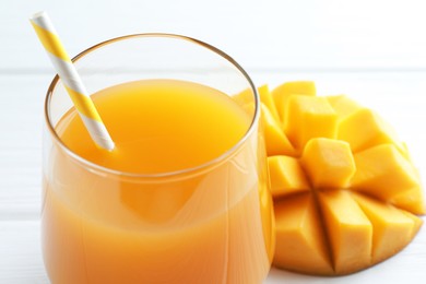 Photo of Tasty mango juice in glass and fresh fruit on white table, closeup