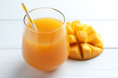 Photo of Tasty mango juice in glass and fresh fruit on white wooden table, closeup