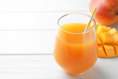 Photo of Tasty mango juice in glass and fresh fruits on white wooden table, closeup. Space for text