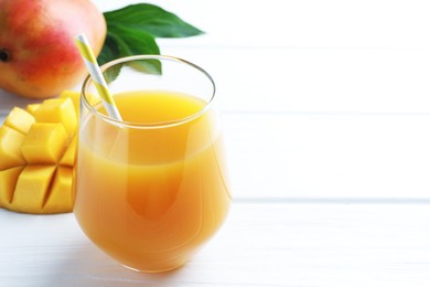 Photo of Tasty mango juice in glass, fresh fruits and green leaves on white wooden table, closeup. Space for text