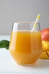 Photo of Tasty mango juice in glass, fresh fruits and green leaves on white wooden table, closeup