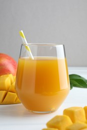 Photo of Tasty mango juice in glass, fresh fruits and green leaves on white wooden table, closeup