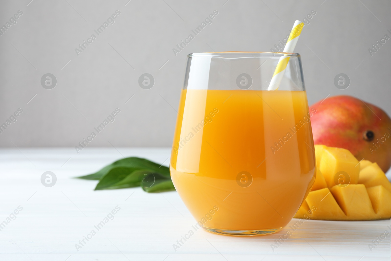 Tasty mango juice in glass, fresh fruits and green leaves on white wooden table, closeup. Space for text Photo of Tasty mango juice in glass, fresh fruits and green leaves on white wooden table, closeup. Space for text