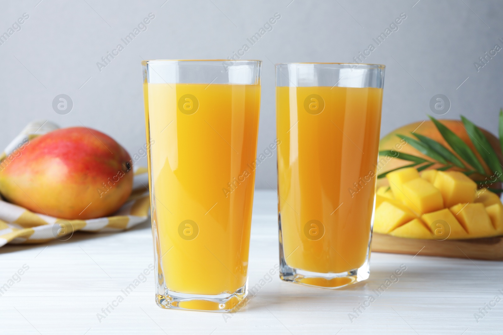Tasty mango juice in glasses, fresh fruits and green leaves on white wooden table, closeup Photo of Tasty mango juice in glasses, fresh fruits and green leaves on white wooden table, closeup