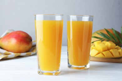 Photo of Tasty mango juice in glasses, fresh fruits and green leaves on white wooden table, closeup
