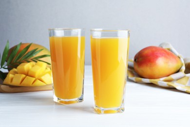 Photo of Tasty mango juice in glasses, fresh fruits and green leaves on white wooden table