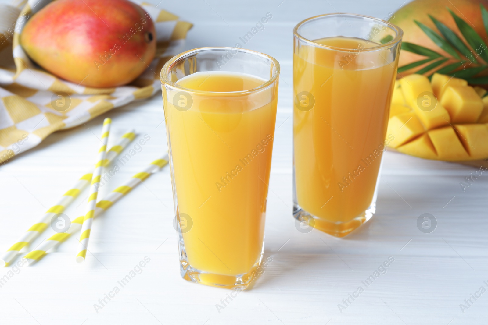 Tasty mango juice in glasses, fresh fruits, straws and green leaves on white wooden table, closeup Photo of Tasty mango juice in glasses, fresh fruits, straws and green leaves on white wooden table, closeup