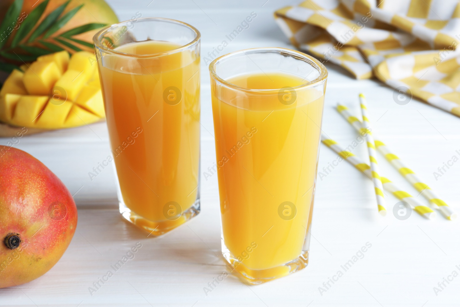 Tasty mango juice in glasses, fresh fruits, straws and green leaves on white wooden table, closeup Photo of Tasty mango juice in glasses, fresh fruits, straws and green leaves on white wooden table, closeup