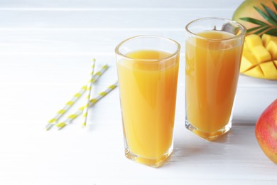 Photo of Tasty mango juice in glasses, fresh fruits, straws and green leaves on white wooden table, closeup