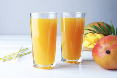 Photo of Tasty mango juice in glasses, fresh fruits, straws and green leaves on white wooden table, closeup