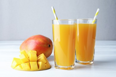 Photo of Tasty mango juice in glasses and fresh fruits on white wooden table, closeup