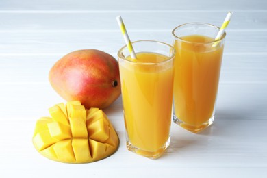 Photo of Tasty mango juice in glasses and fresh fruits on white wooden table, closeup
