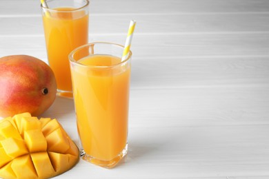 Photo of Tasty mango juice in glasses and fresh fruits on white wooden table, closeup. Space for text
