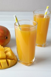 Photo of Tasty mango juice in glasses and fresh fruits on white wooden table, closeup