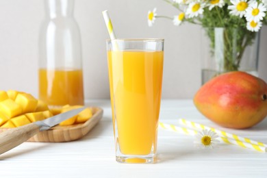 Photo of Tasty mango juice in glass, fresh fruits and chamomile flowers on white wooden table, closeup