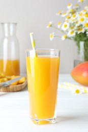 Photo of Tasty mango juice in glass, fresh fruits and chamomile flowers on white wooden table, closeup
