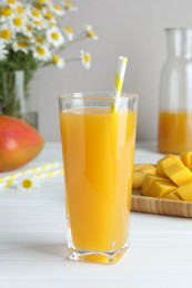Photo of Tasty mango juice in glass, fresh fruits and chamomile flowers on white wooden table, closeup