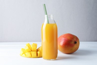 Photo of Tasty mango juice in glass bottle and fresh fruits on white wooden table