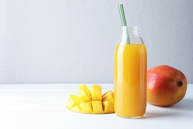 Photo of Tasty mango juice in glass bottle and fresh fruits on white wooden table, space for text