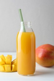 Photo of Tasty mango juice in glass bottle and fresh fruits on white wooden table, closeup