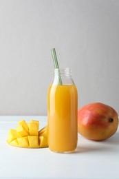 Photo of Tasty mango juice in glass bottle and fresh fruits on white wooden table