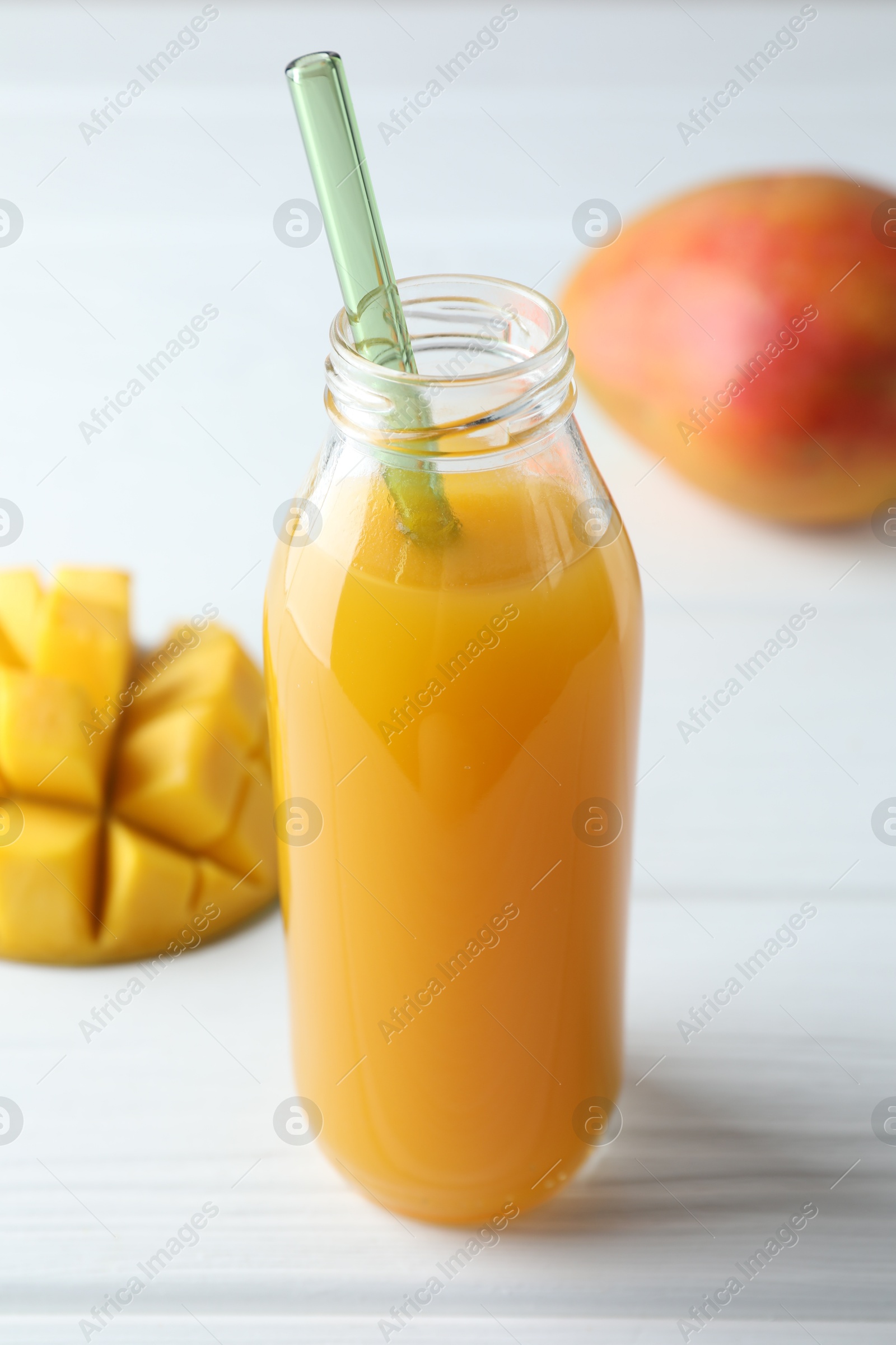Tasty mango juice in glass bottle and fresh fruits on white wooden table, closeup Photo of Tasty mango juice in glass bottle and fresh fruits on white wooden table, closeup
