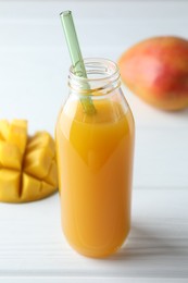 Photo of Tasty mango juice in glass bottle and fresh fruits on white wooden table, closeup