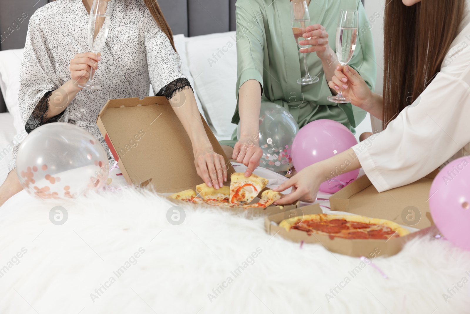 Pajama party. Friends with glasses eating pizza on bed at home, closeup Photo of Pajama party. Friends with glasses eating pizza on bed at home, closeup
