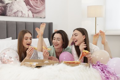 Photo of Pajama party. Happy friends eating pizza on bed at home