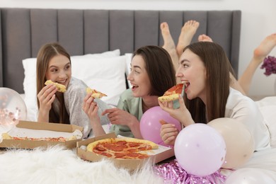 Photo of Pajama party. Happy friends eating pizza on bed at home