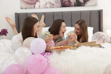 Photo of Pajama party. Happy friends eating pizza on bed at home