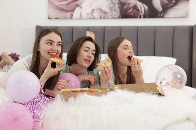 Photo of Pajama party. Happy friends eating pizza on bed at home