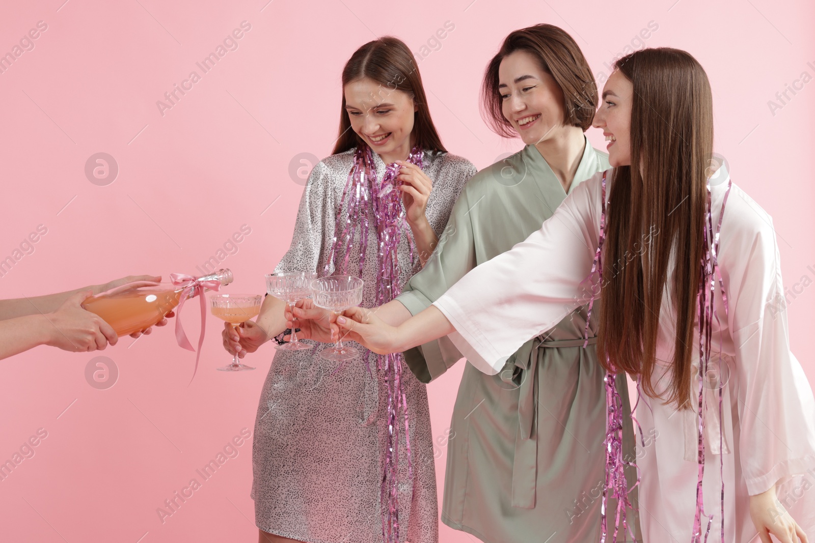 Photo of Pajama day. Woman pouring alcoholic drink for her happy friends on pink background, closeup