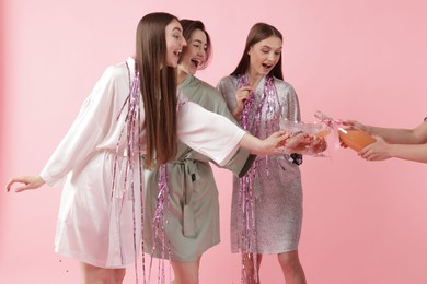 Photo of Pajama day. Woman pouring alcoholic drink for her happy friends on pink background, closeup