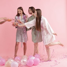 Photo of Pajama day. Woman pouring alcoholic drink for her happy friends on pink background, closeup