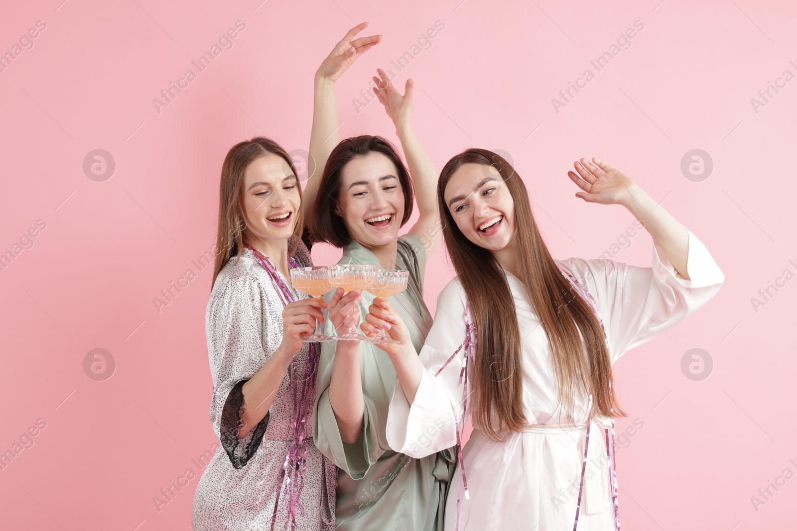 Photo of Pajama party. Happy friends with tinsel clinking glasses on pink background